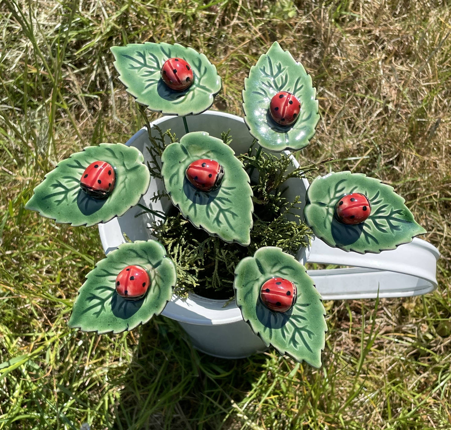 Mariquita de cerámica sobre hoja, flor de cerámica en tallo